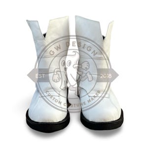 Könnte beinhalten: Ein Paar weiße Lederstiefel mit schwarzen Sohlen. Die Stiefel haben ein einzigartiges Design mit hohem, abgewinkeltem Kragen. Das Bild enthält ein Logo mit der Aufschrift "GW DESIGN CUSTOM COSTUME MAKER EST 2018".