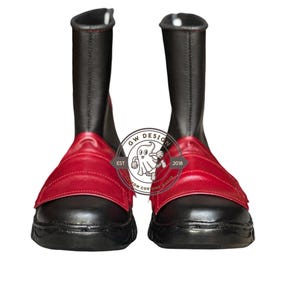 Peut inclure: Paire de bottes noires avec des d&eacute;tails rouges. Les bottes ont une tige haute et une sangle rouge sur le dessus du pied. Les bottes sont en mati&egrave;re lisse. Les bottes sont neuves et pr&eacute;sent&eacute;es sur fond blanc.