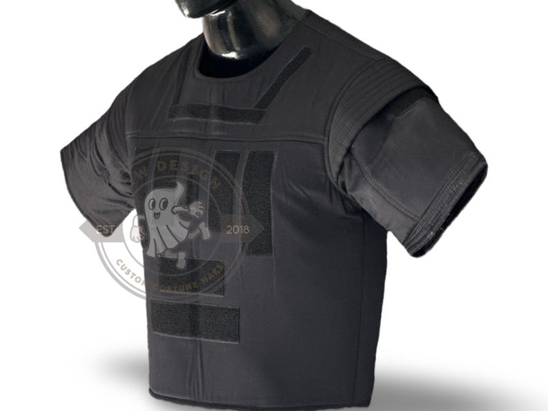 May include: Black tactical vest with padded shoulders and sleeves. The vest features Velcro patches and a round logo with a cartoon ghost and the text "CUSTOM COSTUME WARE" and "2018".
