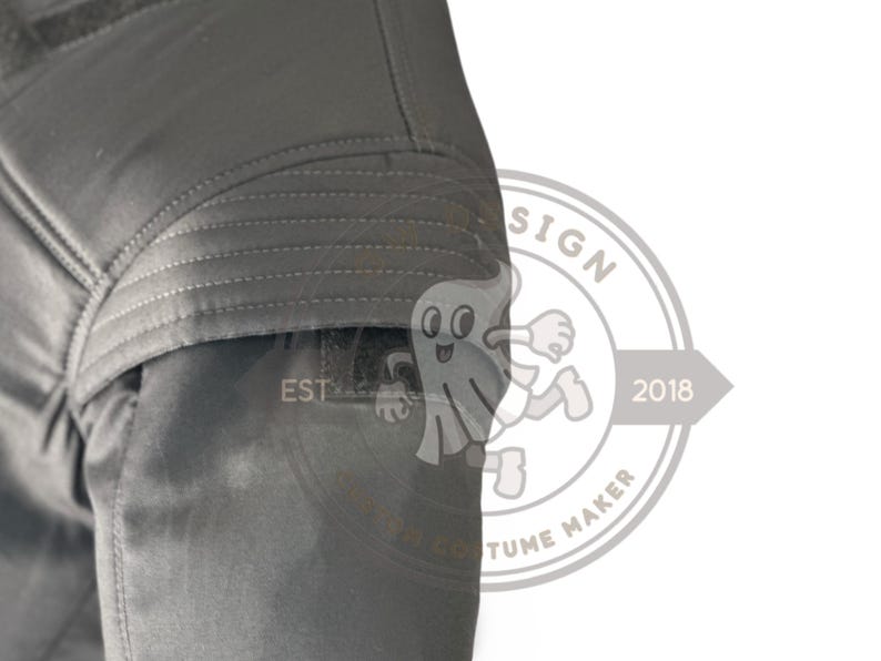 May include: A close-up of a section of a dark grey garment, possibly a jacket or coat, with quilted stitching details. The image includes a portion of a logo with the text "EST" and a cartoon ghost figure.