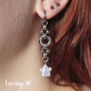 Könnte beinhalten: Silberner Ohrring mit einem sternförmigen Anhänger. Der Ohrring ist an einem Reifen befestigt und verfügt über eine Kette aus miteinander verbundenen Metallringen und Perlen. Der Text "Earrings #1" ist unten links sichtbar.