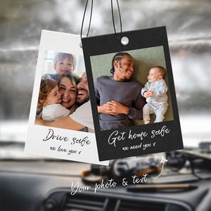 May include: Two car air fresheners with photos. One is white with a family photo and the text "Drive safe, we love you x". The other is black with a father and baby, with the text "Get home safe, we need you x".