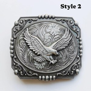 May include: Silver-toned metal belt buckle with an embossed eagle design, wings outstretched. The buckle has an ornate, floral-inspired border and the text "Style 2" in the upper right corner. The eagle is the focal point.