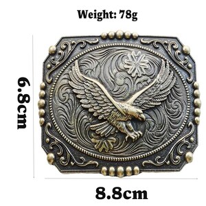 May include: A rectangular, antique-style belt buckle with an eagle design. The buckle is 3.5 inches wide and 2.7 inches tall, with a weight of 2.7 ounces. The eagle is centered, with outstretched wings, and surrounded by ornate scrollwork.