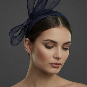 May include: Navy blue headband with a bow and mesh detailing. The headpiece features a structured bow on the front and a delicate mesh accent, suitable for special occasions. The dark blue color adds a touch of elegance.