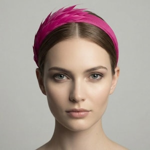 May include: A magenta headband with a textured band and feather detailing. The headband is worn on a person's head, with the feathers positioned on the left side. The background is a solid, neutral gray.