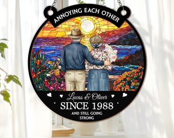 May include: Circular decorative sign featuring an elderly couple in front of a sunset scene. The sign reads "Annoying Each Other" at the top, with "Lucas & Oliver SINCE 1988 AND STILL GOING STRONG" at the bottom. The image has a stained-glass effect.