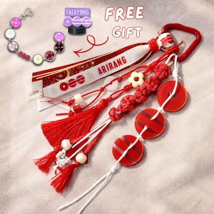 May include: A collection of red and white accessories, including a keychain with a red handle, a bracelet, and a ribbon with the word "ARIRANG". The keychain features red circular charms and a tassel.