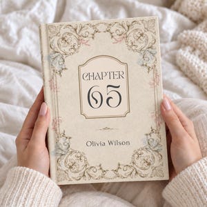May include: A hardcover book with a cream-colored cover featuring ornate floral scrollwork in muted tones of blue, pink, and gold. The center displays the text "CHAPTER 65" in a decorative frame, with the name "Olivia Wilson" printed below it.