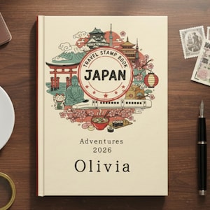 May include: A cream-colored travel stamp book with a colorful illustration of Japanese landmarks and the word "JAPAN" in a circular design. The book is personalized with the name "Olivia" and the year "2026".