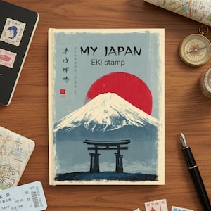 May include: A travel journal titled "MY JAPAN EKI stamp" with a red sun, a snow-capped mountain, and a traditional Japanese gate illustration. The journal is on a wooden surface with a passport, map, compass, and stamps.