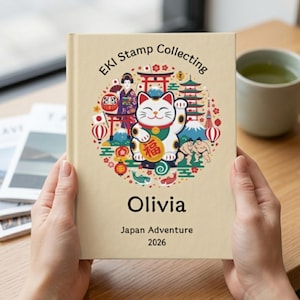May include: A beige journal titled "EKI Stamp Collecting" with a colorful Japanese-themed illustration featuring a lucky cat, pagodas, and sumo wrestlers. The name "Olivia" and "Japan Adventure 2026" are printed below the illustration.