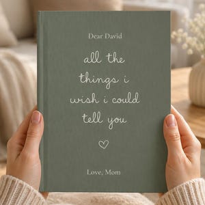 Op de afbeelding: Een saliegroen hardcover boek met witte tekst: Dear David, all the things i wish i could tell you, gevolgd door een klein hartpictogram en de tekst: Love, Mom. De boekomslag heeft een subtiele, fijnkorrelige textuur over het gehele oppervlak.