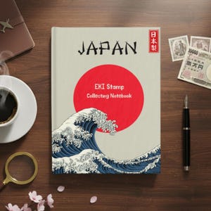 May include: A notebook with "JAPAN" printed on the cover, featuring a red circle and a blue and white wave design. The text "EKI Stamp Collecting Notebook" is also visible. A cup of coffee, a magnifying glass, and a pen are on the wooden surface.