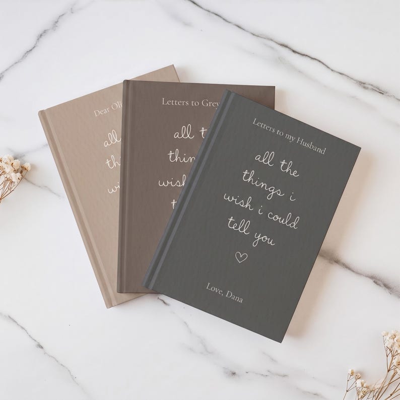 Może przedstawiać: Trzy notatniki w twardej oprawie w kolorze beżowym, taupe i ciemnoszarym. Każda okładka zawiera napis "Letters to my Husband" oraz "all the things i wish i could tell you" białą czcionką, z małym serduszkiem i podpisem "Love, Dana" na dole.