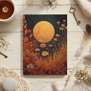 May include: A journal with a full moon and floral design. The cover features a large, golden moon against a dark blue starry sky, with orange and yellow flowers and foliage in the foreground. A cup of tea with a daisy and a vintage key are also in the image.