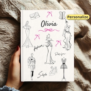 May include: A white notebook with fashion-themed illustrations and the name "Olivia" in black script. The notebook features sketches of dresses, a handbag, bows, and the words "fashion", "design", and "style". The word "Personalize" is in a yellow box.