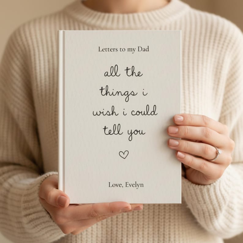 Może przedstawiać: Biała książka w twardej oprawie z czarnym napisem: Letters to my Dad, all the things i wish could tell you, małą ikoną serca oraz tekstem Love, Evelyn. Książka ma prosty, przejrzysty wygląd z okładką o wyczuwalnej, delikatnej fakturze.