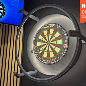 Può includere: Un bersaglio per freccette con un design nero, verde e rosso, montato su un muro. Il bersaglio per freccette è circondato da una cornice metallica. L'immagine include il testo "NEW OMMO DESIGN".