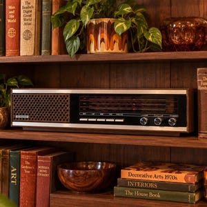 May include: A vintage Kenwood stereo receiver with a dark wood cabinet, a black front panel featuring a radio frequency display, a perforated speaker grille, and three silver control knobs, positioned on a wooden shelf among various books.