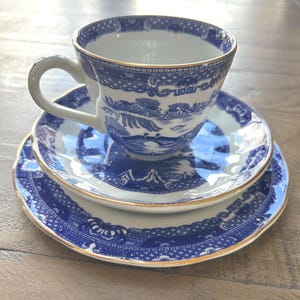 Peut inclure: Service à thé en porcelaine bleu et blanc. La tasse et les soucoupes présentent un motif paysager détaillé avec des bordures dorées. L'ensemble comprend une tasse, une petite soucoupe et une grande assiette, toutes avec des motifs assortis.