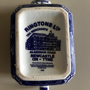 Peut inclure: Une bo&icirc;te &agrave; th&eacute; rectangulaire en c&eacute;ramique avec un motif bleu et blanc. La base porte l'inscription RINGTONS LTD TEA MERCHANTS, ALGERNON ROAD NEWCASTLE ON TYNE, PRODUCED BY WADE CERAMICS, BASED UPON AN ORIGINAL MALING TEA POT, 1996.
