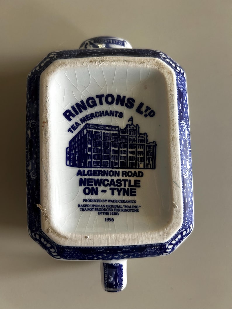 Peut inclure: Une bo&icirc;te &agrave; th&eacute; rectangulaire en c&eacute;ramique avec un motif bleu et blanc. La base porte l'inscription RINGTONS LTD TEA MERCHANTS, ALGERNON ROAD NEWCASTLE ON TYNE, PRODUCED BY WADE CERAMICS, BASED UPON AN ORIGINAL MALING TEA POT, 1996.