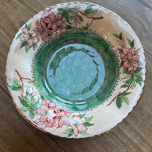Puede incluir: Un cuenco decorativo de cerámica con un diseño floral. El cuenco presenta flores rosas, hojas verdes y un borde dorado. El interior tiene un patrón verde y azul. El cuenco es probablemente vintage o antiguo.