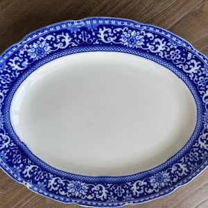 May include: Oval serving platter with a white centre and a blue floral border. The blue border features intricate patterns and a scalloped edge. This decorative dish is ideal for serving food.