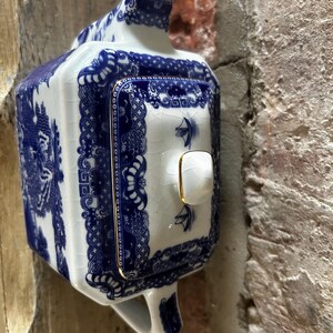 Peut inclure: Une th&eacute;i&egrave;re rectangulaire en c&eacute;ramique avec une base blanche orn&eacute;e de motifs bleus complexes de style willow et une finition &eacute;maill&eacute;e craquel&eacute;e. Le couvercle poss&egrave;de un petit bouton blanc avec un bord dor&eacute;, assorti &agrave; la bordure dor&eacute;e du couvercle.