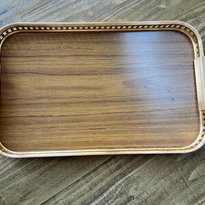 May include: A rectangular serving tray featuring a smooth, medium-brown wood grain base. The tray is enclosed by a metallic gold-toned frame with a decorative beaded edge and two flat, vertical handles on the left and right sides.