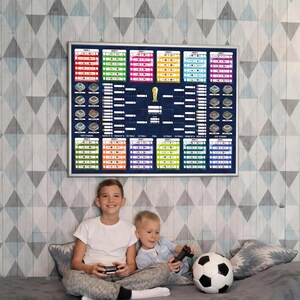 May include: A rectangular wall poster featuring a colorful soccer tournament bracket with group stages, knockout rounds, and a central trophy icon, displayed in a silver frame. The design includes various team slots and stadium illustrations.