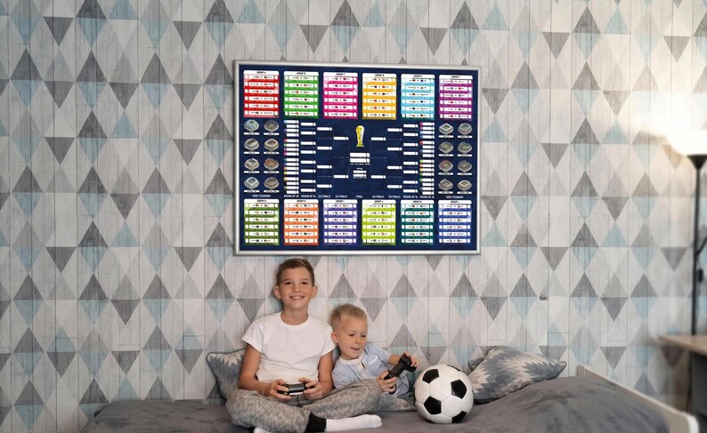 May include: A rectangular wall poster featuring a colorful soccer tournament bracket with group stages, knockout rounds, and a central trophy icon, displayed in a silver frame. The design includes various team slots and stadium illustrations.