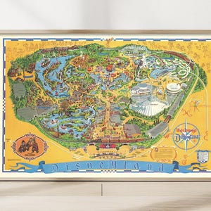 May include: A framed vintage map of Disneyland, featuring a detailed illustration of the park's attractions. The map is set against a yellow background with a blue banner that reads "Disneyland". The map is in a wooden frame.