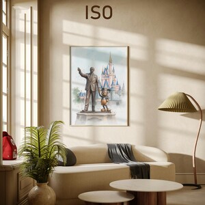 May include: A framed watercolor print featuring a statue of Walt Disney with Mickey Mouse in front of a castle. The print hangs above a beige sofa with a gray throw, and two round coffee tables with wooden legs.