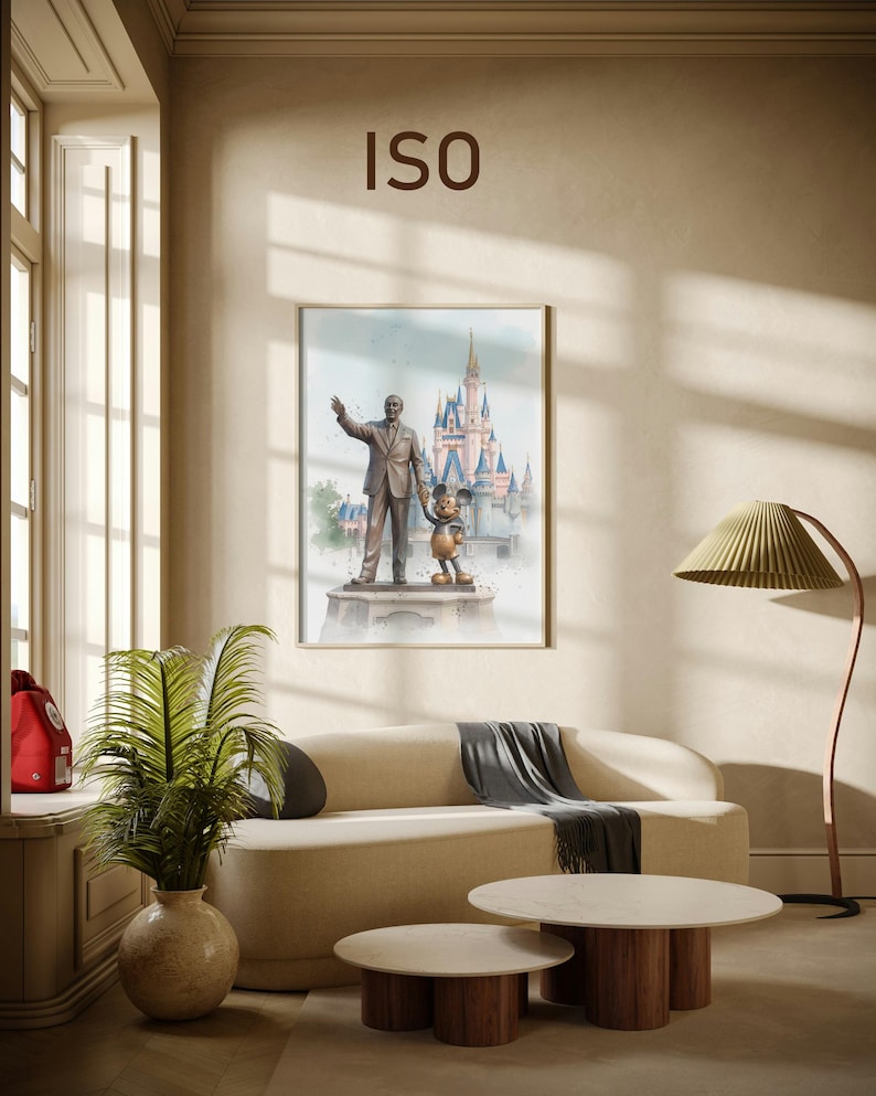 May include: A framed watercolor print featuring a statue of Walt Disney with Mickey Mouse in front of a castle. The print hangs above a beige sofa with a gray throw, and two round coffee tables with wooden legs.