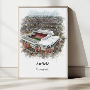 May include: Watercolor-style print of Anfield stadium in Liverpool, England. The artwork depicts an aerial view of the stadium with a red and green field, surrounded by buildings and trees. The text "Anfield Liverpool" is at the bottom.