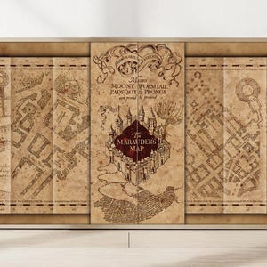 May include: A framed print of The Marauder's Map, a fictional map from the Harry Potter series. The map is in shades of brown and tan, with detailed illustrations of a castle and surrounding areas. The text includes the names of the map's creators and the title, "The Marauder's Map."