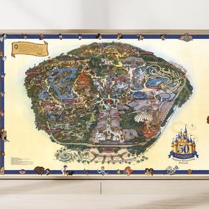 May include: A framed vintage-style map of a theme park, featuring detailed illustrations of attractions and landmarks. The map is bordered with character illustrations and includes text indicating a 50th-anniversary celebration.