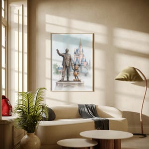 May include: A framed watercolor print featuring a statue of Walt Disney with Mickey Mouse in front of a castle. The artwork is displayed above a beige sofa with a gray throw, and two round coffee tables.