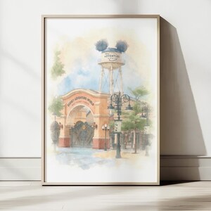 Op de afbeelding: Een aquarel kunstdruk met de toegangspoort van Disney Adventure World, voorzien van een beige boog, een hoge watertoren met Mickey Mouse-oren, sierlijke zwarte metalen hekken en lantaarnpalen tegen een zachte blauwe en gele lucht.