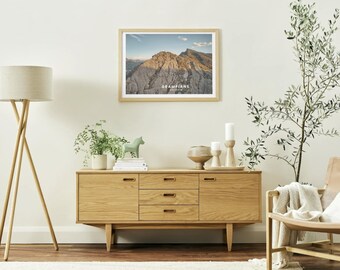 May include: A framed landscape print of the Grampians mountain range hangs above a wooden cabinet. The cabinet has three drawers and two doors. A floor lamp and decorative items, including a green horse figurine, are also visible.