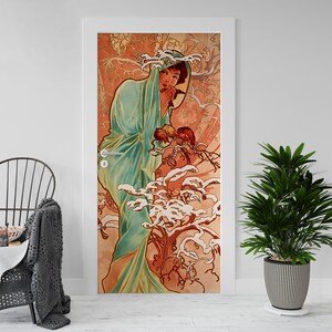 Op de afbeelding: Een decoratieve deurwrap met een illustratie in Art Nouveau-stijl. Het kunstwerk toont een vrouw in een vloeiende turquoise jurk, omringd door gestileerde bloemen en boomachtige elementen in tinten oranje, bruin en wit. De deur is wit omlijst.