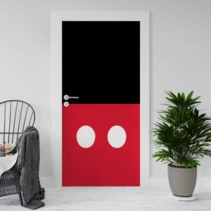 Op de afbeelding: Een deur met een zwart bovenstuk en een rood onderstuk, met twee witte cirkels. De deur is wit omlijst en heeft een zilveren handgreep. Een kamerplant in een patroonpot staat rechts.