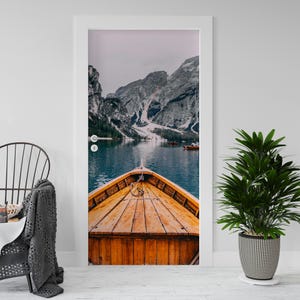 Op de afbeelding: Een deurwrap met een serene meerzicht met een houten boot. Het dek van de boot is warm bruin, afstekend tegen het koele blauwe water en de met sneeuw bedekte bergen op de achtergrond. De afbeelding roept een gevoel van vrede en rust op.