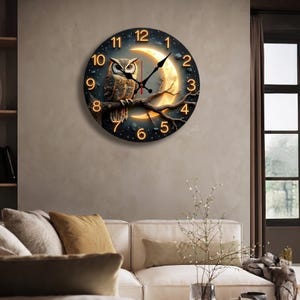 May include: A round wall clock featuring an owl perched on a branch in front of a crescent moon. The clock face is black with gold numerals and hands. The owl has brown and white feathers. The clock is a decorative item.