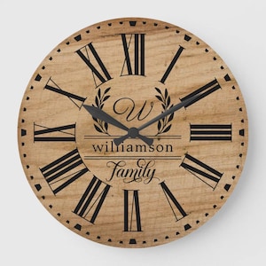 Puede incluir: Un reloj de pared redondo de madera con números romanos y manecillas negras. La esfera del reloj presenta el nombre "Williamson Family" en una fuente decorativa, con una "W" y una corona de laurel.