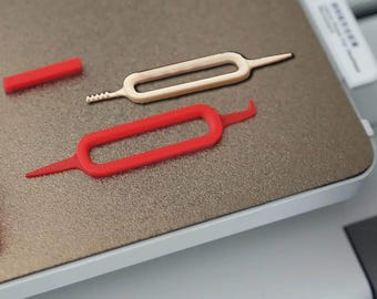 May include: An image showing three small plastic tools. Two are red, and one is off-white. The tools have a rectangular shape with a loop in the middle and pointed ends. One red tool has a hook-shaped end.