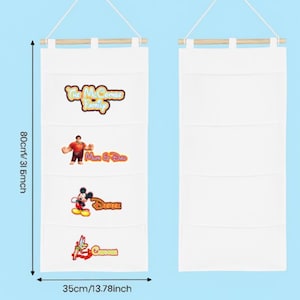 Könnte beinhalten: Weißer Stoff-Hängeorganizer mit vier Taschen, 80 cm lang und 35 cm breit. Mit Disney-Charaktergrafiken und Text. Enthält eine Holzstange und eine Schnur zum Aufhängen.
