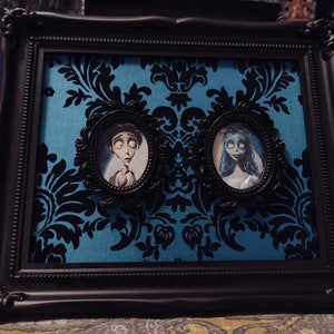 May include: A black framed picture with a blue and black patterned background. Two smaller frames with portraits of a man and a woman are inside the larger frame.